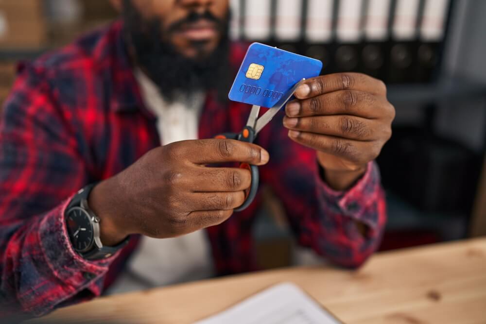 african american man in a red plaid shirt cutting up a blue credit card