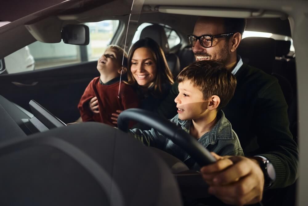 Happy parents and their kids having fun while testing new car in a showroom