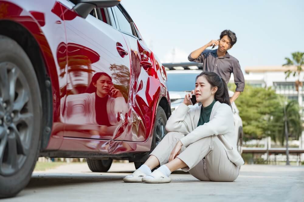 Two people calling for help after a car accident, showing a damaged vehicle