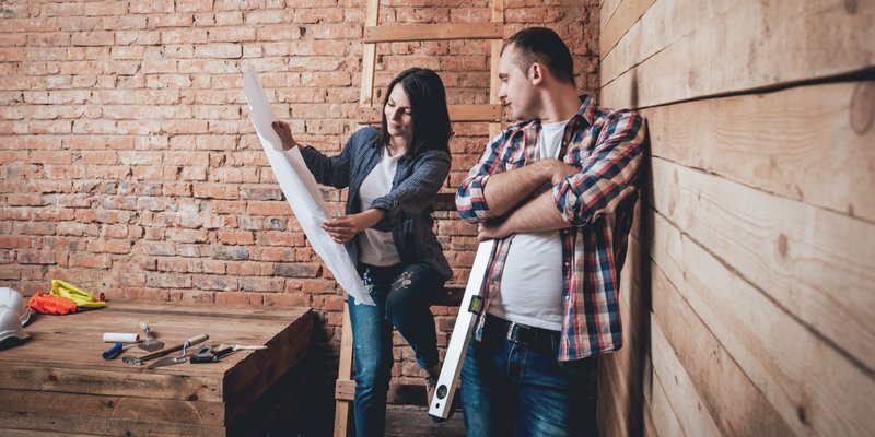 A woman holds blueprints open to show a man during a home renovation