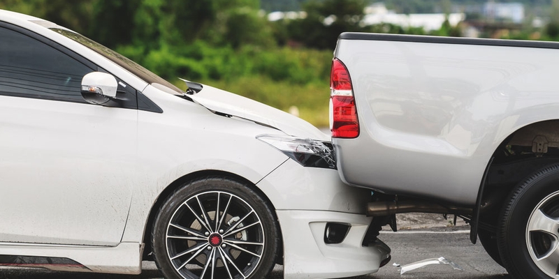 A white car rear-ends a pickup truck in a collision/car accident, and is damaged