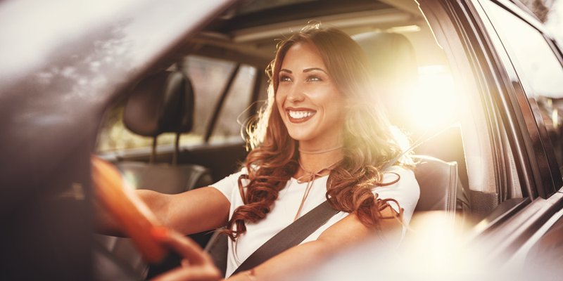 A young woman drives with the sun reflecting behind her