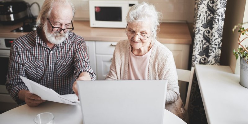 An older couple reviewing paperwork and working on a laptop