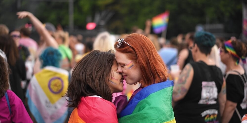 two women embracing at pride in berlin draped in a rainbow flag
